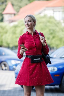 Güzel sarışın kadının içinde kırmızı elbise holding hareket eden telefon, açık moda portre sokak arka plan bulanık 