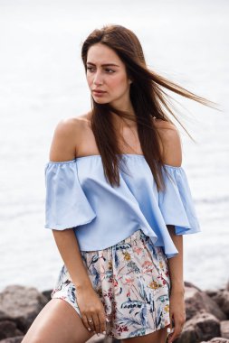 Şort ve tişört ayakta gündüz kayalık kumsalda giyen güzel genç kahverengi saçlı kadın açık atış