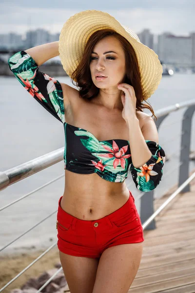 カラフルな夏服美容ブルネット モデルの屋外のポートレート 昼間にぼかした背景に堤防の上に立って若い美しい女性 — ストック写真