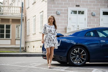 Çiçekler beyaz elbiseli güzel genç kadın açık bir kadeh. Gündüz, modern spor araba Caddesi üzerinde yakın kadın modeli ayakta