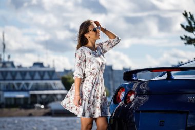 Çiçekler beyaz elbiseli güzel genç kadın açık bir kadeh. Gündüz, modern spor araba Caddesi üzerinde yakın kadın modeli ayakta