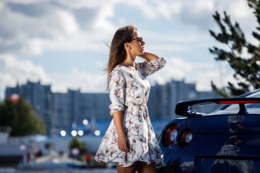 Çiçekler beyaz elbiseli güzel genç kadın açık bir kadeh. Gündüz, modern spor araba Caddesi üzerinde yakın kadın modeli ayakta