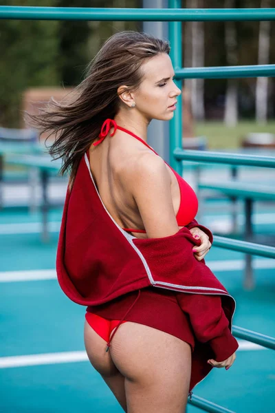 白天站在运动区的美丽年轻女子身穿红色泳衣和红色头套的户外肖像 — 图库照片