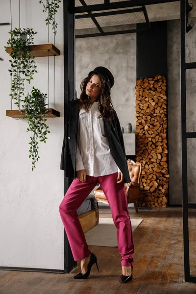 Fashion portrait of beauty brunette model wearing black jacket, white shirt and pink pants. Young beautiful woman posing in luxury apartments interior