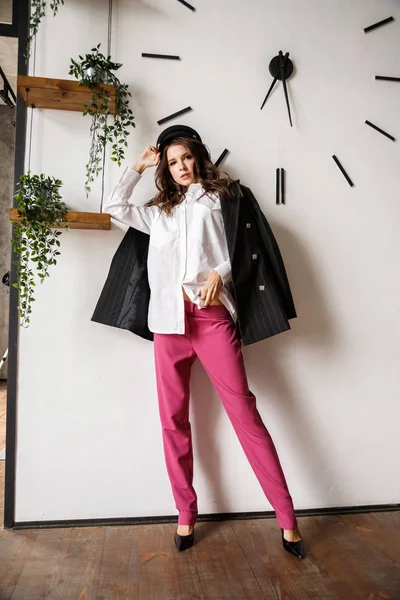 Fashion portrait of beauty brunette model wearing black jacket, white shirt and pink pants. Young beautiful woman posing in luxury apartments interior