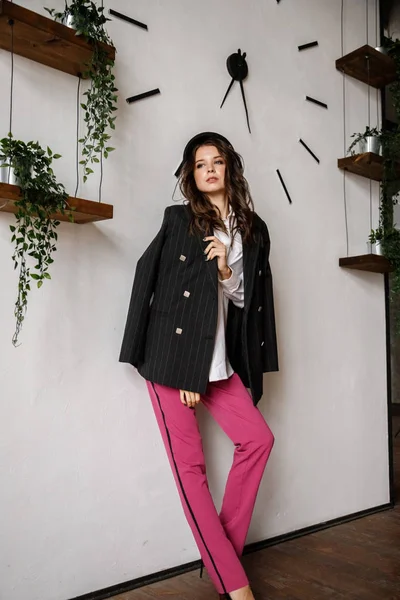 Fashion portrait of beauty brunette model wearing black jacket, white shirt and pink pants. Young beautiful woman posing in luxury apartments interior