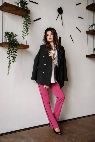 Fashion portrait of beauty brunette model wearing black jacket, white shirt and pink pants. Young beautiful woman posing in luxury apartments interior