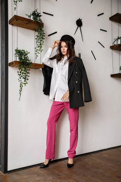 Fashion portrait of beauty brunette model wearing black jacket, white shirt and pink pants. Young beautiful woman posing in luxury apartments interior