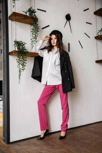 Fashion portrait of beauty brunette model wearing black jacket, white shirt and pink pants. Young beautiful woman posing in luxury apartments interior