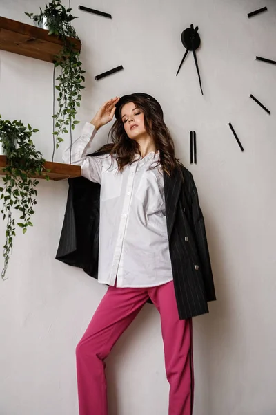 Fashion portrait of beauty brunette model wearing black jacket, white shirt and pink pants. Young beautiful woman posing in luxury apartments interior