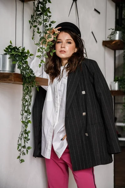 Fashion portrait of beauty brunette model wearing black jacket, white shirt and pink pants. Young beautiful woman posing in luxury apartments interior