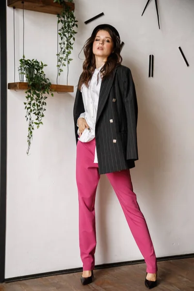 Fashion portrait of beauty brunette model wearing black jacket, white shirt and pink pants. Young beautiful woman posing in luxury apartments interior