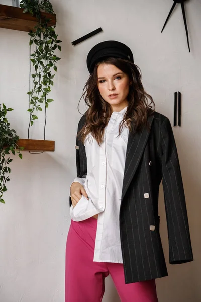 Fashion portrait of beauty brunette model wearing black jacket, white shirt and pink pants. Young beautiful woman posing in luxury apartments interior