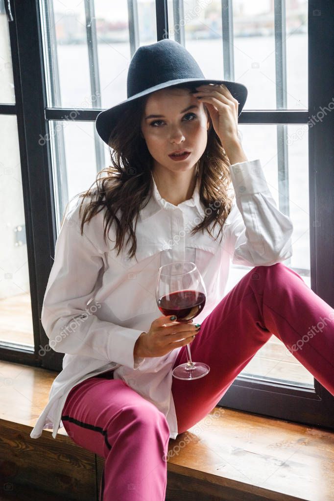 Fashion portrait of beauty brunette model wearing white shirt and pink pants. Young beautiful woman posing in luxury apartments interior