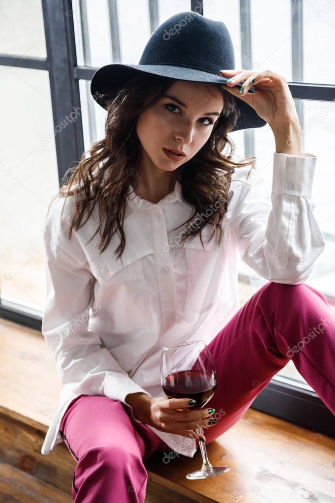 Fashion portrait of beauty brunette model wearing white shirt and pink pants. Young beautiful woman posing in luxury apartments interior