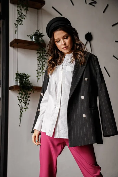 Fashion portrait of beauty brunette model wearing black jacket, white shirt and pink pants. Young beautiful woman posing in luxury apartments interior