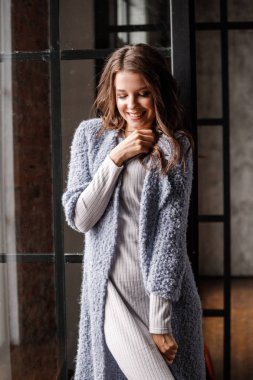 Güzellik kadın modeli giymiş beyaz portre elbise ve mavi ceket. Lüks daireler iç pencereye yakın duran kıvırcık esmer kadın