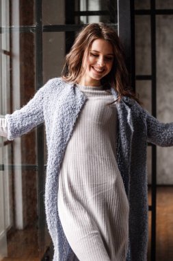 Güzellik kadın modeli giymiş beyaz portre elbise ve mavi ceket. Lüks daireler iç pencereye yakın duran kıvırcık esmer kadın