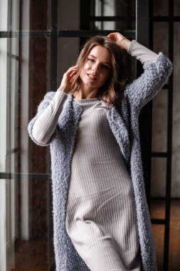 Güzellik kadın modeli giymiş beyaz portre elbise ve mavi ceket. Lüks daireler iç pencereye yakın duran kıvırcık esmer kadın
