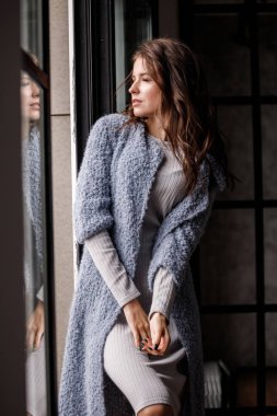 Güzellik kadın modeli giymiş beyaz portre elbise ve mavi ceket. Lüks daireler iç pencereye yakın duran kıvırcık esmer kadın