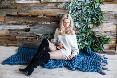 Stüdyo beyaz kazak giyen güzellik kadın portresi. Mavi örme halı, ahşap duvar arka plan üzerinde oturan kadın modeli