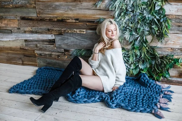 Stüdyo beyaz kazak giyen güzellik kadın portresi. Mavi örme halı, ahşap duvar arka plan üzerinde oturan kadın modeli