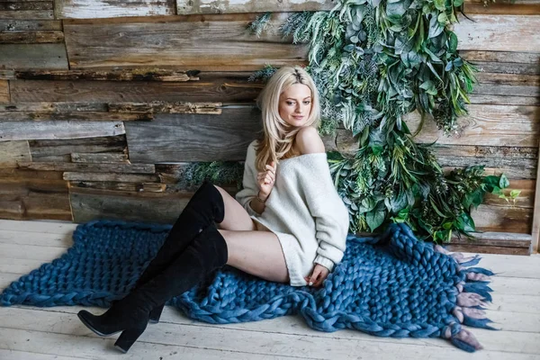 Stüdyo beyaz kazak giyen güzellik kadın portresi. Mavi örme halı, ahşap duvar arka plan üzerinde oturan kadın modeli