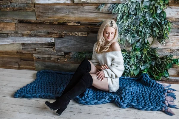 白のセーターを着ている金髪美女のスタジオの肖像画 青いニット カーペット 木製の壁の背景の上に座っている女性モデル — ストック写真