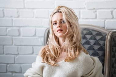 Stüdyo beyaz kazak giyen güzellik kadın portresi. Şık makyaj koltuğu, tuğla duvar arka plan oturan kadın modeli