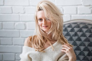 Stüdyo beyaz kazak giyen güzellik kadın portresi. Şık makyaj koltuğu, tuğla duvar arka plan oturan kadın modeli