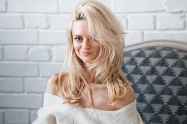 Stüdyo beyaz kazak giyen güzellik kadın portresi. Şık makyaj koltuğu, tuğla duvar arka plan oturan kadın modeli