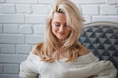 Stüdyo beyaz kazak giyen güzellik kadın portresi. Şık makyaj koltuğu, tuğla duvar arka plan oturan kadın modeli