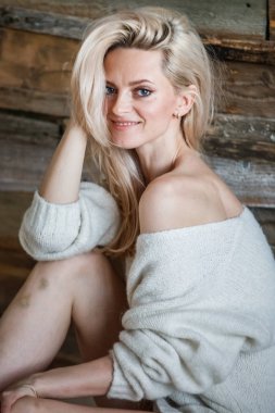 Stüdyo beyaz kazak giyen güzellik kadın portresi. Ahşap katta oturan kadın modeli 