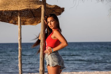 Güzel esmer model gündüz kumsalda duran kırmızı mayo ve kot şort