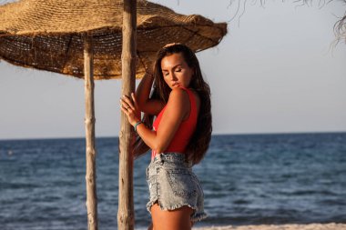 Güzel esmer model gündüz kumsalda duran kırmızı mayo ve kot şort