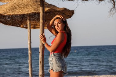 Güzel esmer model gündüz kumsalda duran kırmızı mayo ve kot şort