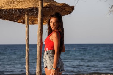 Güzel esmer model gündüz kumsalda duran kırmızı mayo ve kot şort