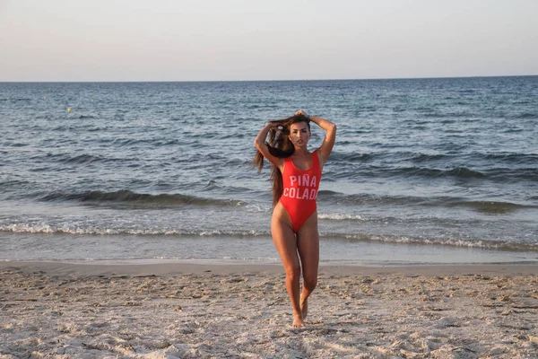 白天穿着红色泳衣站在沙滩上的年轻黑发妇女 — 图库照片