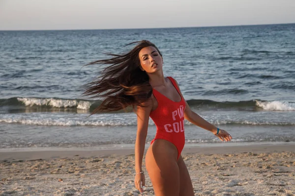 赤い水着立っている身に着けている砂浜のビーチで昼間に若いブルネットの女性 — ストック写真