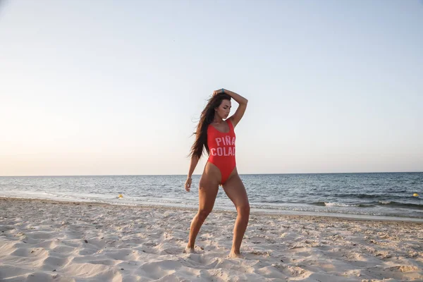 白天穿着红色泳衣站在沙滩上的年轻黑发妇女 — 图库照片