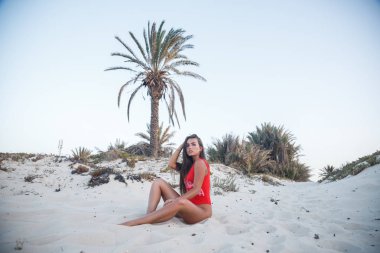 Gündüz kumlu plaj üzerinde oturan kırmızı mayo giyen genç esmer kadın