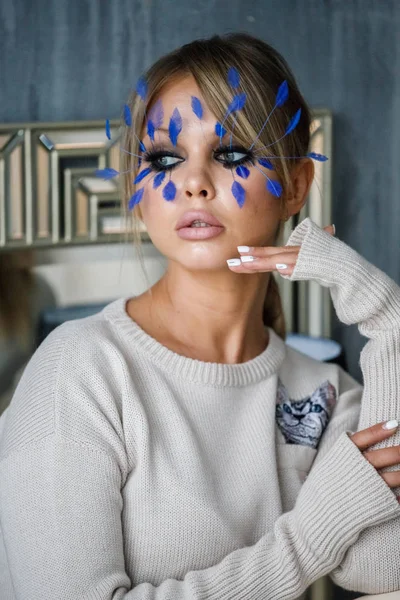 Lüks daire iç, Beyaz giysili güzel sarışın kadın. Yüzündeki küçük mavi tüyleri ile şık makyaj modeliyle Güzellik Portresi