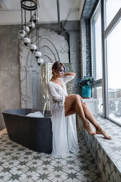 可爱的金发碧眼的女人在豪华浴室内饰白色的衣服 美丽的模型的肖像与时尚的化妆与小蓝色羽毛在脸上 — 图库照片