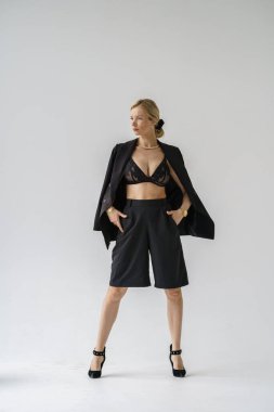 Beyaz arka planda izole edilmiş seksi sarışın modelin şık bir portresi. Siyah günlük giysiler ve stüdyoda poz veren siyah iç çamaşırlı genç bir model.