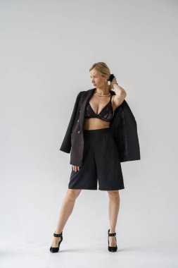 Beyaz arka planda izole edilmiş seksi sarışın modelin şık bir portresi. Siyah günlük giysiler ve stüdyoda poz veren siyah iç çamaşırlı genç bir model.