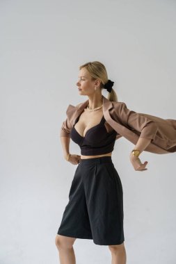 Beyaz arka planda izole edilmiş seksi sarışın modelin şık bir portresi. Bej ceketli genç bir manken ve stüdyoda poz veren siyah günlük kıyafetler.