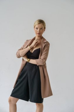 Beyaz arka planda izole edilmiş seksi sarışın modelin şık bir portresi. Bej ceketli genç bir manken ve stüdyoda poz veren siyah günlük kıyafetler.