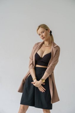 Beyaz arka planda izole edilmiş seksi sarışın modelin şık bir portresi. Bej ceketli genç bir manken ve stüdyoda poz veren siyah günlük kıyafetler.