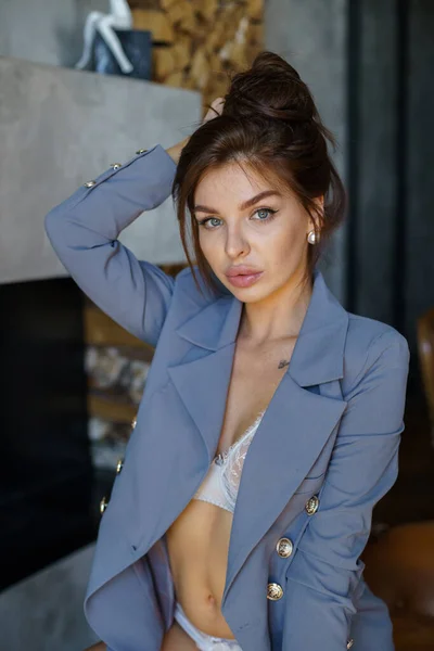 Sexual brunette model with tattoos on body posing at luxury apartments interior. Studio portrait of young woman wearing white lingerie and blue jacket