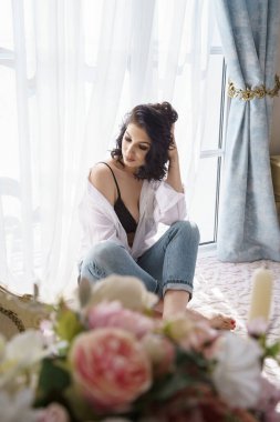 Dairelerin içinde poz veren güzel kıvırcık esmer. Mavi kot ve beyaz gömlekli genç modelin portresi. 